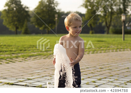 Cute baby boy playing with water jet in park fountain Cute baby boy playing with water jet in park fountain 42894788