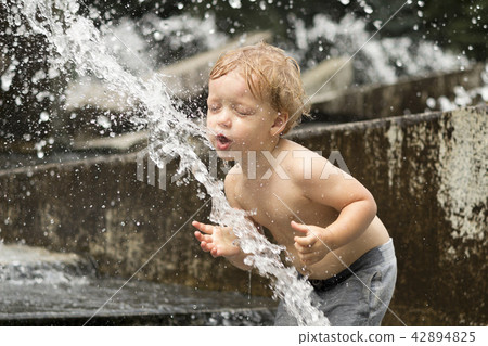 Funny baby boy trying to cauch water stream in fountain. Cute toddler playing in the city fountain. Funny baby boy trying to cauch water stream in fountain. Cute toddler playing in the city fountain. 42894825