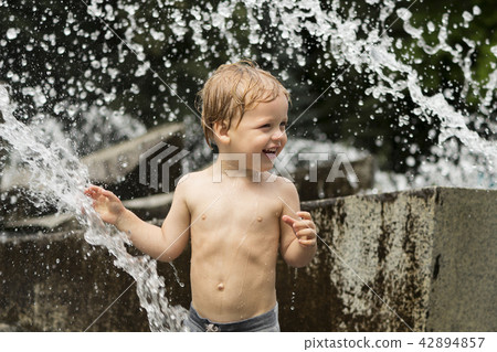Funny smiling baby boy trying to cauch water stream in fountain. Cute toddler playing in the city Funny smiling baby boy trying to cauch water stream in fountain. Cute toddler playing in the city 42894857
