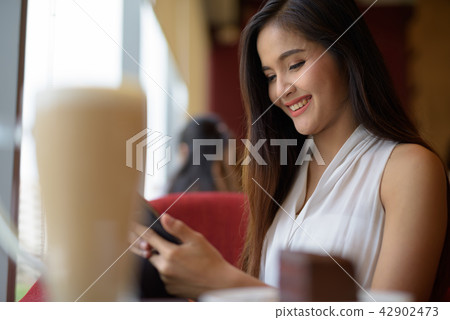 Young beautiful Asian businesswoman relaxing at the coffee shop Young beautiful Asian businesswoman relaxing at the coffee shop 42902473
