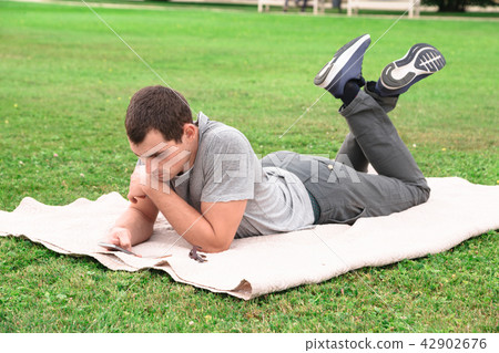 Man lying on blanket on grass with mobile Man lying on blanket on grass with mobile 42902676