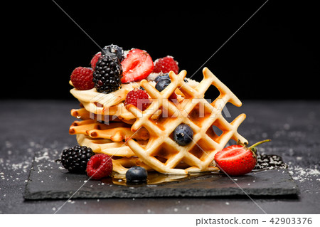 Photo of fresh viennese wafers with berries with powdered sugar on blackboard on blank background 42903376