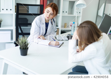 A beautiful young girl in a white robe is sitting at the desk in the office and communicating with A beautiful young girl in a white robe is sitting at the desk in the office and communicating with 42904058