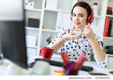 Beautiful young girl sitting in headphones at desk in office eating yogurt with red filling. 42904083