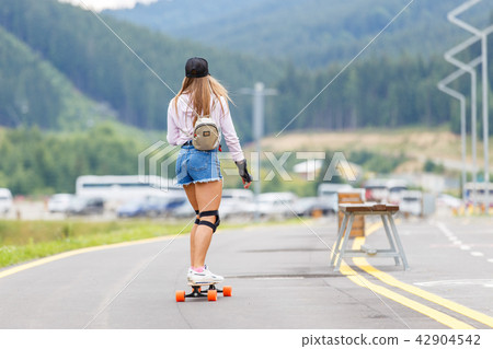 Young girl with pads longboarding on hillside road Young girl with pads longboarding on hillside road 42904542