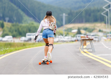 Young girl with pads longboarding on hillside road Young girl with pads longboarding on hillside road 42904543