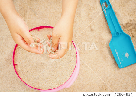 hands of a girl with sand over a colored bucket and shovel on the beach hands of a girl with sand over a colored bucket and shovel on the beach 42904934