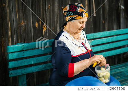 old woman is sitting on a bench and is cutting green apples old woman is sitting on a bench and is cutting green apples 42905108