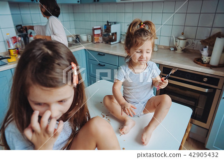 Two little girls in the kitchen sitting on the table. Two little girls in the kitchen sitting on the table. 42905432
