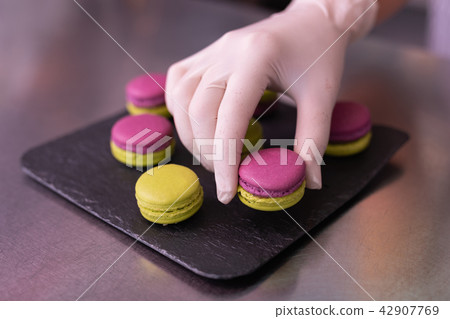 Master of confectionary putting nice macaroons on black plate Master of confectionary putting nice macaroons on black plate 42907769