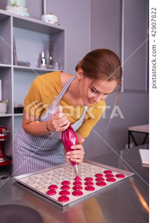 Appealing woman wearing grey apron working with pastry bag Appealing woman wearing grey apron working with pastry bag 42907822