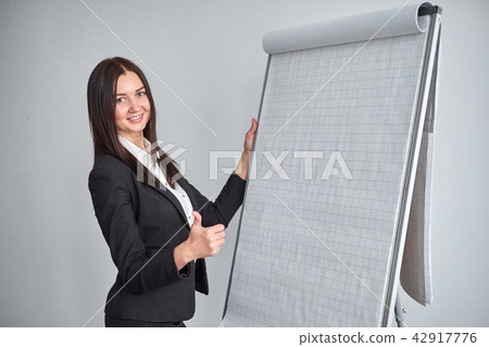 Portrait of young smiling businesswoman standing by flipchart in office Portrait of young smiling businesswoman standing by flipchart in office 42917776