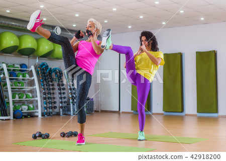 Two fit women doing straight leg kicking exercise while working-out in gym Two fit women doing straight leg kicking exercise while working-out in gym 42918200
