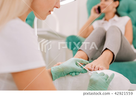 Blonde-haired chiropodist wearing gloves making pedicure Blonde-haired chiropodist wearing gloves making pedicure 42921559