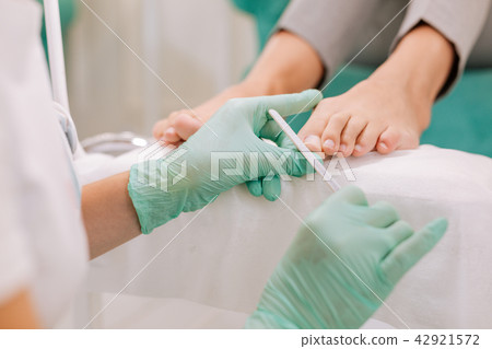 Professional chiropodist using file while making pedicure Professional chiropodist using file while making pedicure 42921572