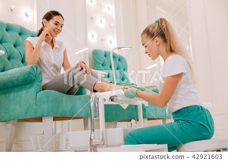 Dark-haired woman sitting in comfortable armchair getting pedicure Dark-haired woman sitting in comfortable armchair getting pedicure 42921603