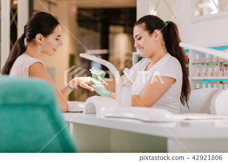 Dark-haired nail master with long ponytail using file making manicure Dark-haired nail master with long ponytail using file making manicure 42921806