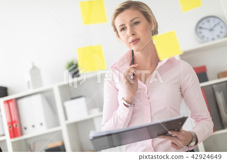 A young blonde girl stands in the office next to a transparent board with stickers and holds A young blonde girl stands in the office next to a transparent board with stickers and holds 42924649