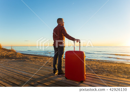 Nature, travel, people concept - a man standing near the sea with red suitcase Nature, travel, people concept - a man standing near the sea with red suitcase 42926130