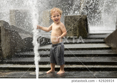 Funny baby boy trying to cauch water stream in fountain. Cute toddler playing in the city fountain. Funny baby boy trying to cauch water stream in fountain. Cute toddler playing in the city fountain. 42926914