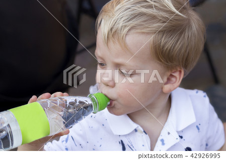 Funny two year baby boy is drinking water from a bottle. 42926995
