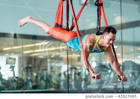 Fit handsome man smiling while practicing anti-gravity yoga 42927485