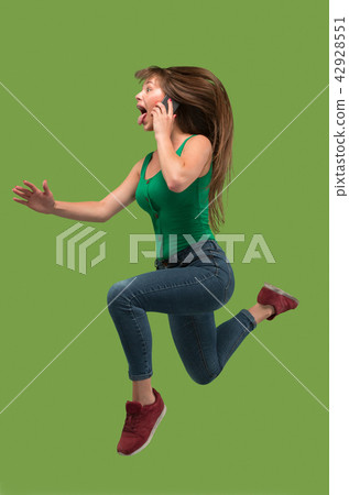 Full length of pretty young woman with mobile phone while jumping Full length of pretty young woman with mobile phone while jumping 42928551