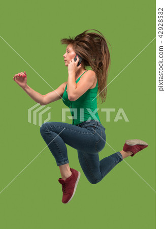 Full length of pretty young woman with mobile phone while jumping 42928582