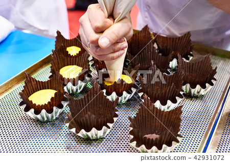 Baker pushes dough into paper muffin forms Baker pushes dough into paper muffin forms 42931072