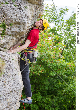 Photo of sportsman in yellow helmet clambering over rock against background of green trees 42931757