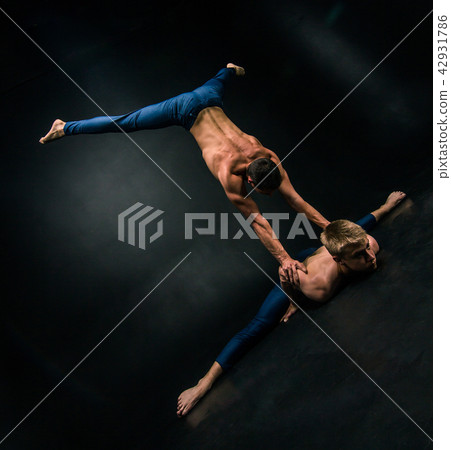Male acrobatic duo performs a complicated balancing act on a dark background 42931786