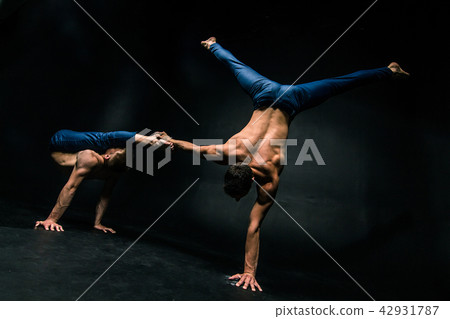 Male acrobatic duo performs a complicated balancing act on a dark background 42931787