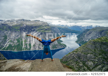 Gymnast standing on his hands on the edge with fjord on background near Trolltunga. Norway 42932973
