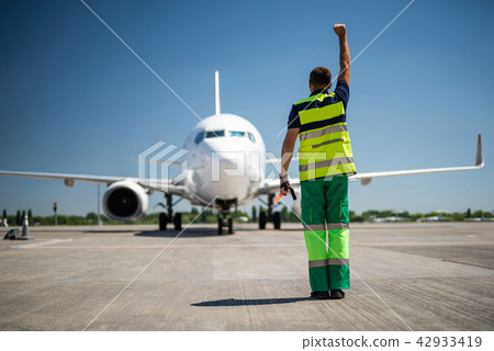 Airport worker raising hand and directing passenger plane in right position 42933419