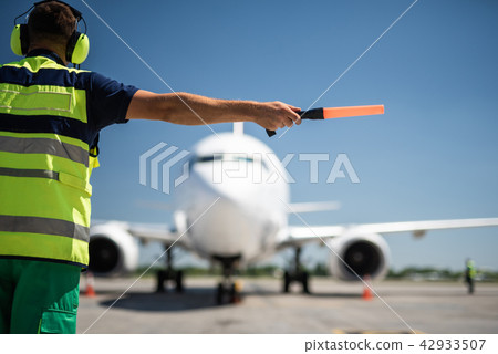 Aviation marshall in headphones directing passenger plane 42933507
