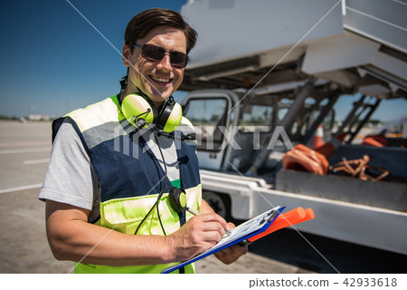 Laughing airport worker holding clipboard, pen and signal wands Laughing airport worker holding clipboard, pen and signal wands 42933618