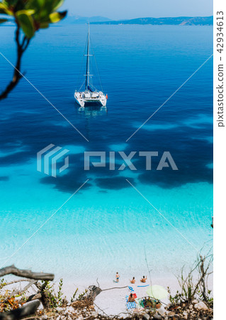 White catamaran yacht at anchor on clear azure surface with dark pattern in calm blue lagoon 42934613