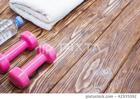 dumbbells and a bottle of water with towel on wooden background, concept preparing to fitness sports 42935092