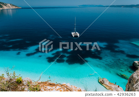 White catamaran yacht at anchor in calm clear azure water lagoon. Unrecognizable tourists relax and White catamaran yacht at anchor in calm clear azure water lagoon. Unrecognizable tourists relax and 42936263