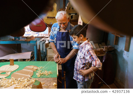 Old Lute Maker Teaching Grandson Boy Chiseling Wood Old Lute Maker Teaching Grandson Boy Chiseling Wood 42937136