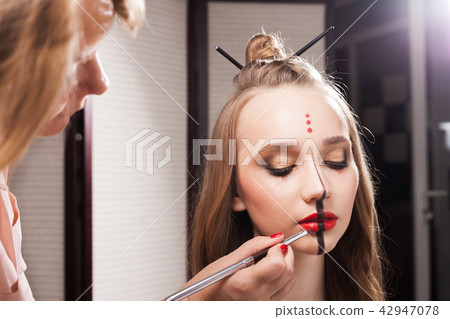stylist applying lip gloss on a model with unusual makeup stylist applying lip gloss on a model with unusual makeup 42947078