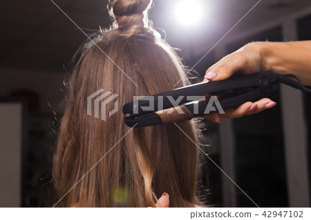 hairdresser curling a hair strand of a girl hairdresser curling a hair strand of a girl 42947102