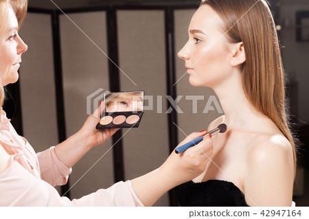 makeup artist applying a concealer on a clavicle of a girl 42947164