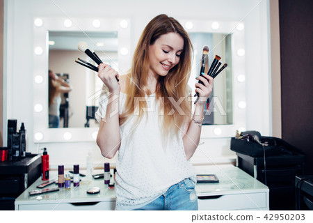 Young shy beautician posing with make-up brushes Young shy beautician posing with make-up brushes 42950203