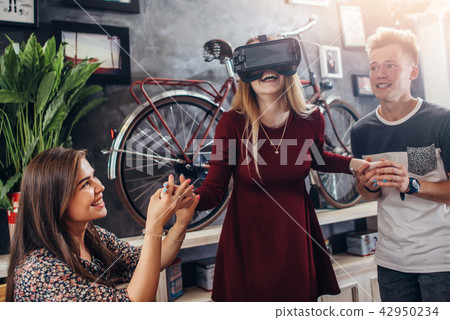 Excited young woman playing interactive videogame wearing virtual reality headset with friends 42950234