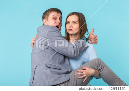 Joking funny couple - girl keeping her boyfriend on her hands over blue background Joking funny couple - girl keeping her boyfriend on her hands over blue background 42951161