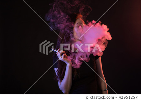 Young woman in neon light and smoke of e-cigarettes or vape on black background Young woman in neon light and smoke of e-cigarettes or vape on black background 42951257