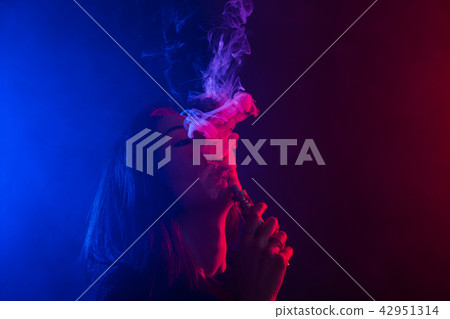 Young woman in neon light and smoke of e-cigarettes or vape on dark background Young woman in neon light and smoke of e-cigarettes or vape on dark background 42951314