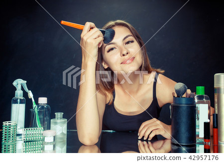 Beauty woman applying makeup. Beautiful girl looking in the mirror and applying cosmetic with a big 42957176