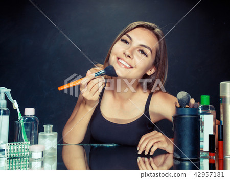 Beauty woman applying makeup. Beautiful girl looking in the mirror and applying cosmetic with a big 42957181